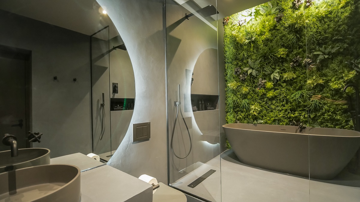 grey freestanding bath with large round mirrors and a biophilic green wall behind the bath