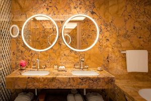 yellow gold marble clad bathroom with round backlit mirrors