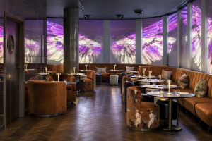 leather banquettes and seating around round table and marble surfaces on a wooden floor with projected images from nature as an installation on the walls