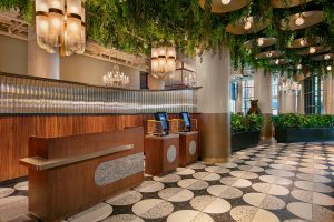 moxy hotel lobby with black and white tiled floor, wooden reception desk and ceiling covered with plants