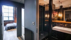 view from bathroom with black tiles and Lusso finishes through the door to industrial style loft apartment