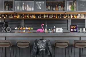 Grey and black bar with leather jacket slung over a bar stool and a signature pink flamingo at Moxy Tromso Sky Bar