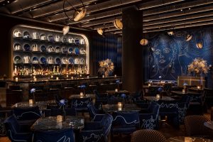 dark blue Silver Lining bar in moxy hotel with candlelight on the tables and a painted mural on the wall