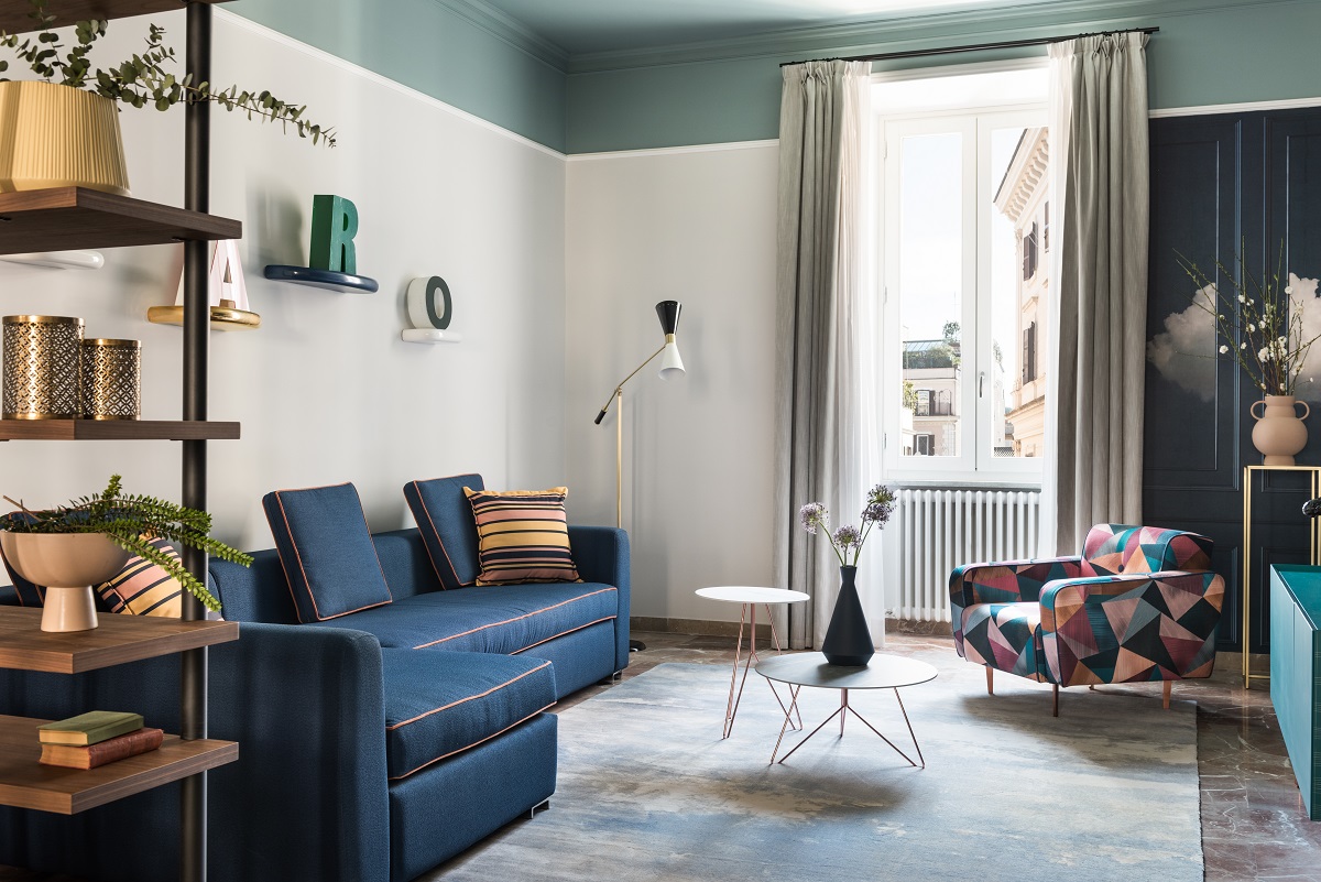 blue l-shaped couch with shelving and patterend focus chair in living room of THDP apartment in Rome