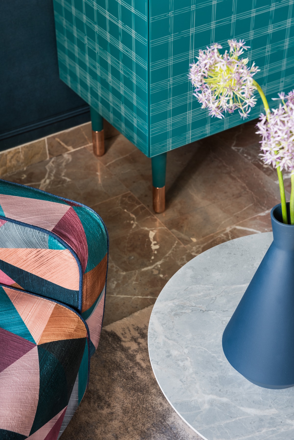 detail of corner of colourful chair, marble flooring, blue cabinet and table with flowers