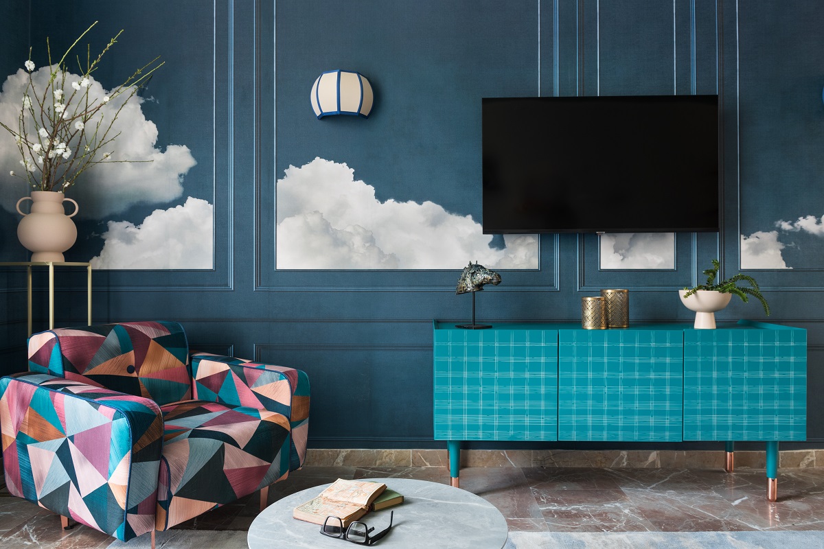 teal walls with cloud mural behind bright patterend upholstered chair and blue mid century cabinet in bright roman interior