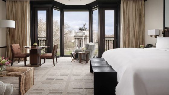 white linen bed dark wood details and panoramic view over central London park from The Peninsula London Park room