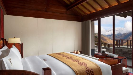 bed with white linen and yellow throw facing window overlooking mountains in guestroom at Ritz-Carlton Reserve in China