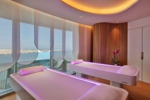 spa beds in room with curved glass windows overlooking ocean and curved statement lighting on the ceiling