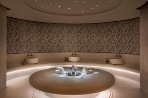 gold and sand coloured patterned mosaics around circular seating and table in the hammam in the Waldorf Astoria Doha spa