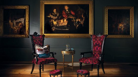 black wall with period paintings in gold frames behind black and red ststement chairs in room designed by Blackpop