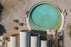aerial view of circular concrete swimming pool set in the sand alongside the arches of the buildings at Casona Sforza
