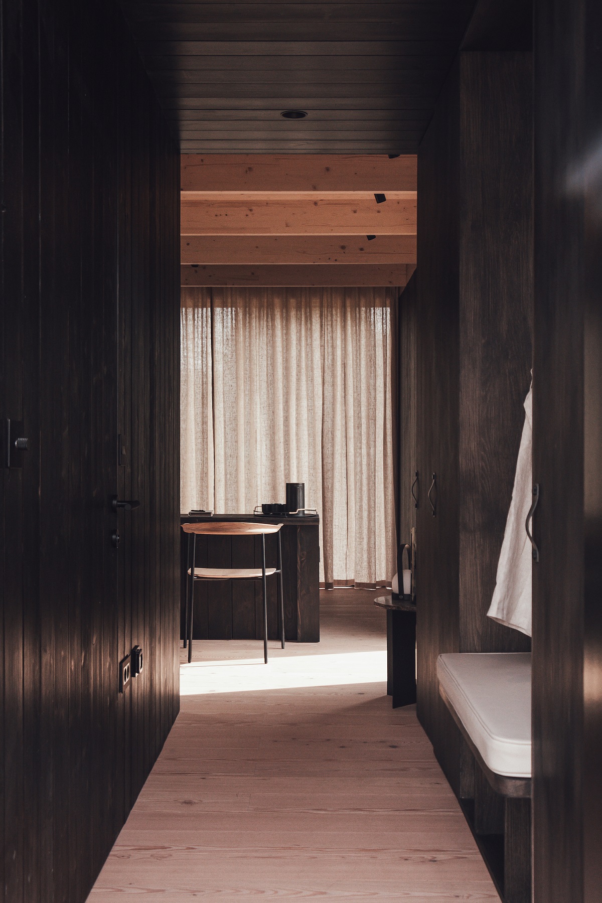 view down corridor in a cabin with wooden floor and dark wood wall panelling though to the bedroom