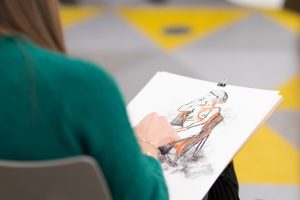 woman in green jumper drawing in a life drawing class with a sketch on her lap