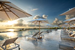 white umbrellas and sunloungers around a swimming pool with tiled surround facing sunrise over the ocean in Emerald Resort Zanzibar