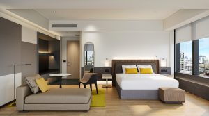 suite in COMO singapore with seating and bed in natural colours with yellow accents and windows on one side with views over the city