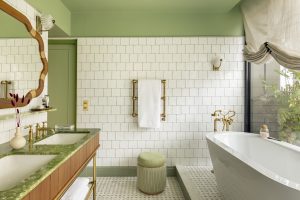 green and white ensuite bathroom with green marble on the vanity and freestanding bath next to window looking onto green plants outside on terrace