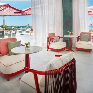 red wicker chair with white cushions on a white floor with view outside to red and white striped parasols