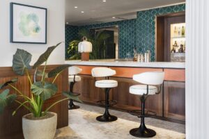 cream bar stools in front of wood and terracotta bar with a green tiled back wall