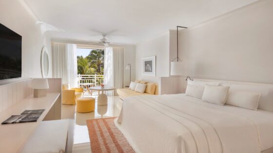 white bed in a white room with white furniture and fittings and doors opening onto balcony and greenery at LUX* Belle Mare, Mauritius