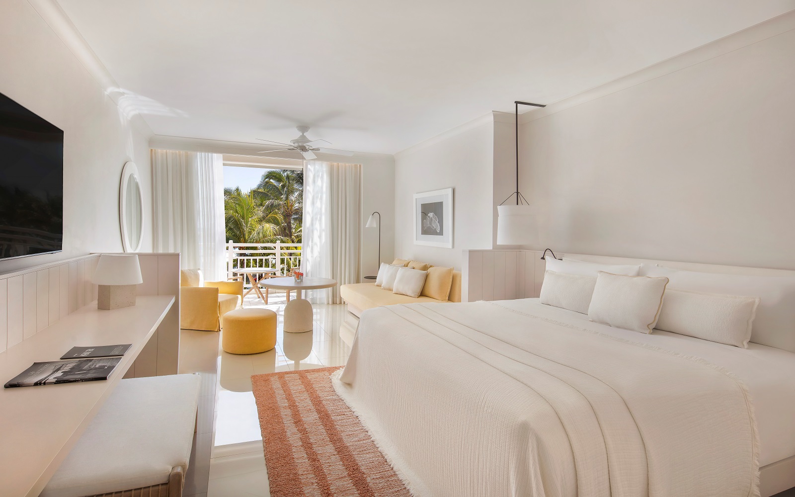 white bed in a white room with white furniture and fittings and doors opening onto balcony and greenery at LUX* Belle Mare, Mauritius