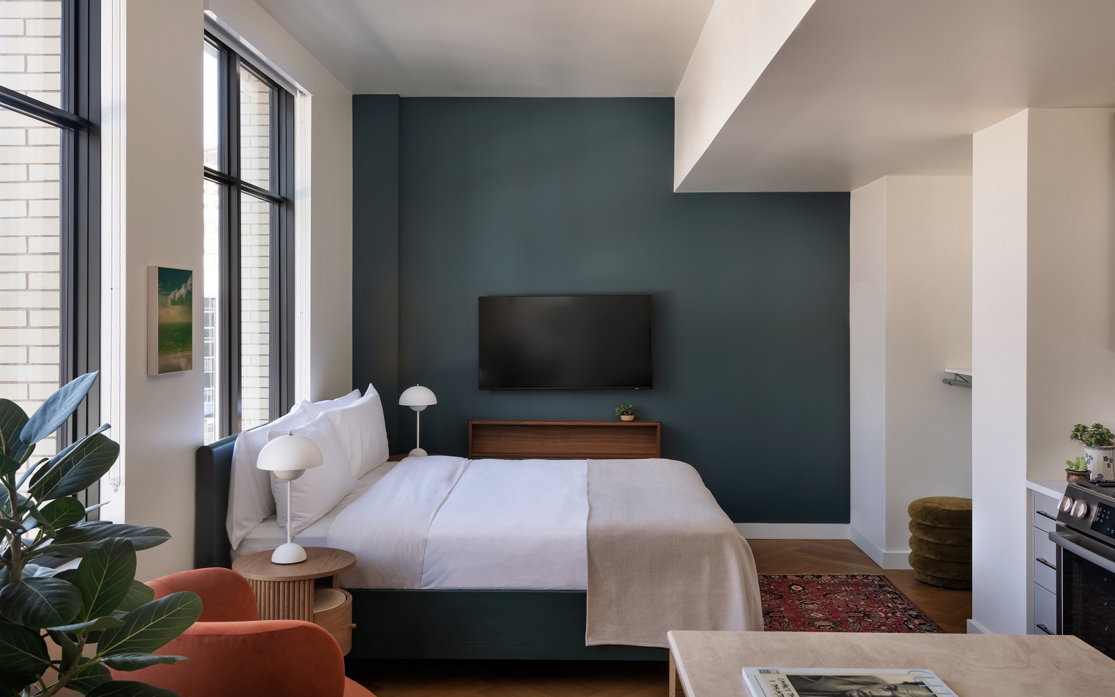 aparthotel guestroom suite with bed in front of dark blue wall and plants in the foreground