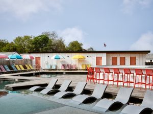 swimming pool with loungers in the water, striped umbrellas and a built bar with orange chairs