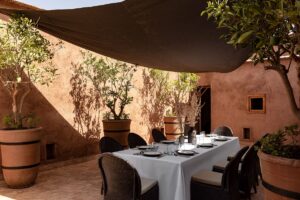 table set for dinner in a clay courtyard with olive trees and a sail shaped shade cloth