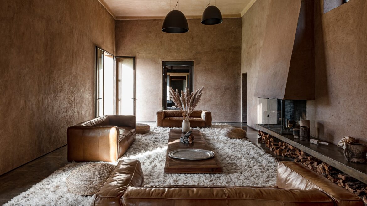 lounge in moroccan house with clay walls and cream wall carpet with leather sofas and natural fibre lampshades