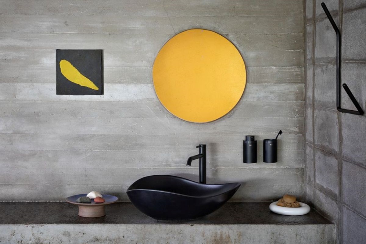 black curved basin from Roca on top of concrete vanity with minimalist yellow decorative elements
