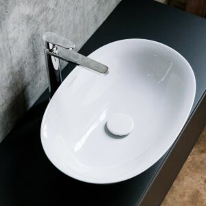 white oval handbasin in black vanity against a concrete wall