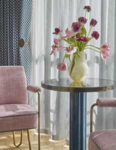 round table with tulips and pink chairs with hairpin legs in front of patterned curtains and window