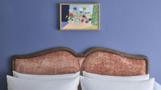 blue wall and coral upholstered headboard with white pillows and art on the wall at the Broadwick Soho