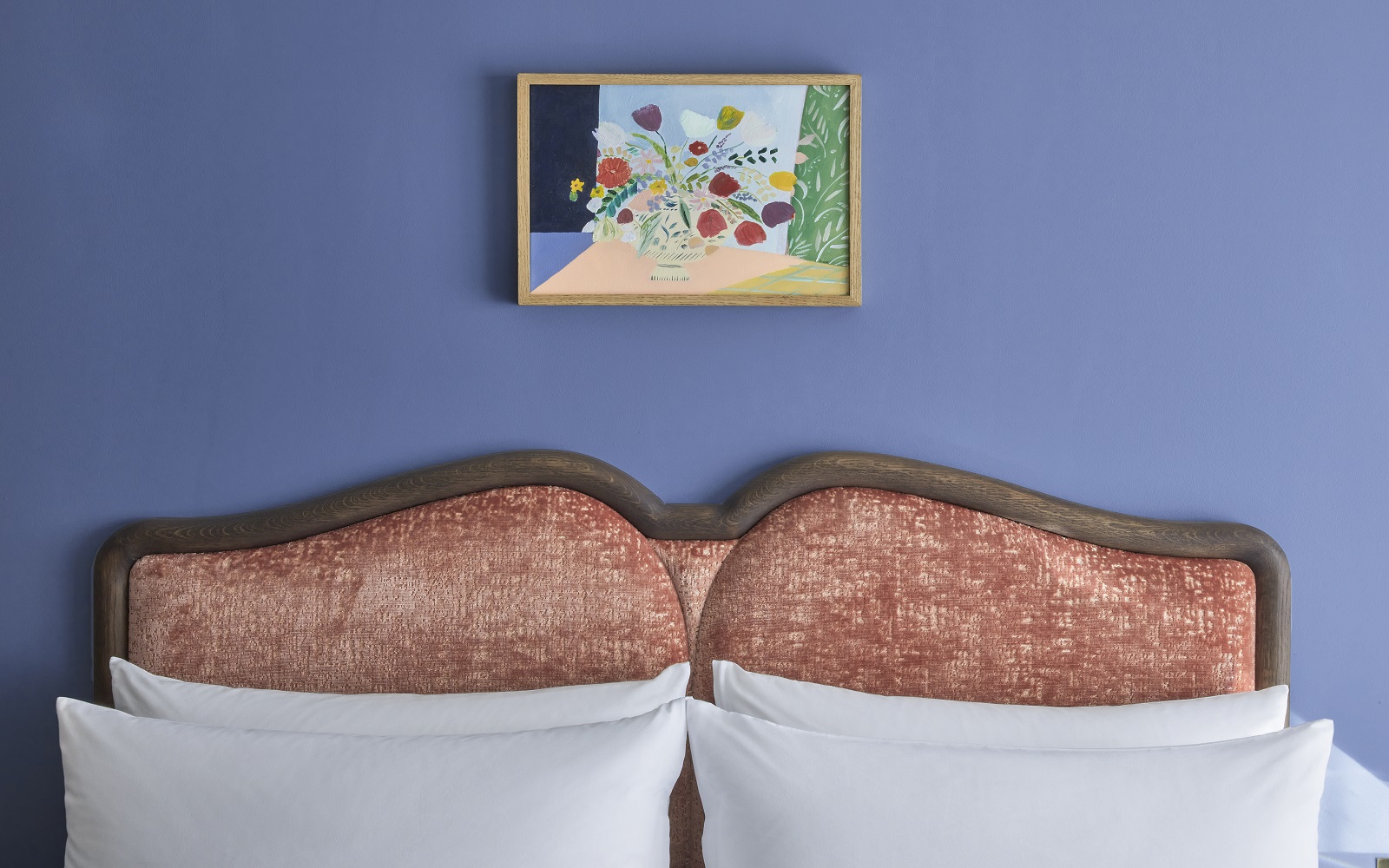 blue wall and coral upholstered headboard with white pillows and art on the wall at the Broadwick Soho