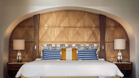 Maroma hotel bed set into arched alcove with a wicker woven headboard behind, blue striped pillows and ceramic bedside lamps