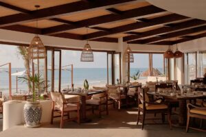 restaurant with seaviews, wooden beams, rattan lampshades and wooden tables and chairs in a mexican aesthetic