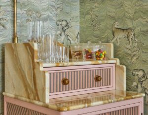 pink and marble desk with jars of sweets and bar accessories against a olive green jungle print wallpaper