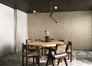 round wooden dining table with wood and rattan chairs and a contemporary wooden lightfitting in front of Arte wallcovering in stone colour