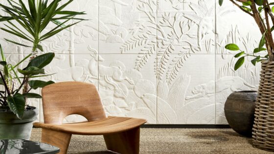 low wooden chair and plants in front of a relief design wallcovering in white showing plants and animals from the mythical babylon by Arte