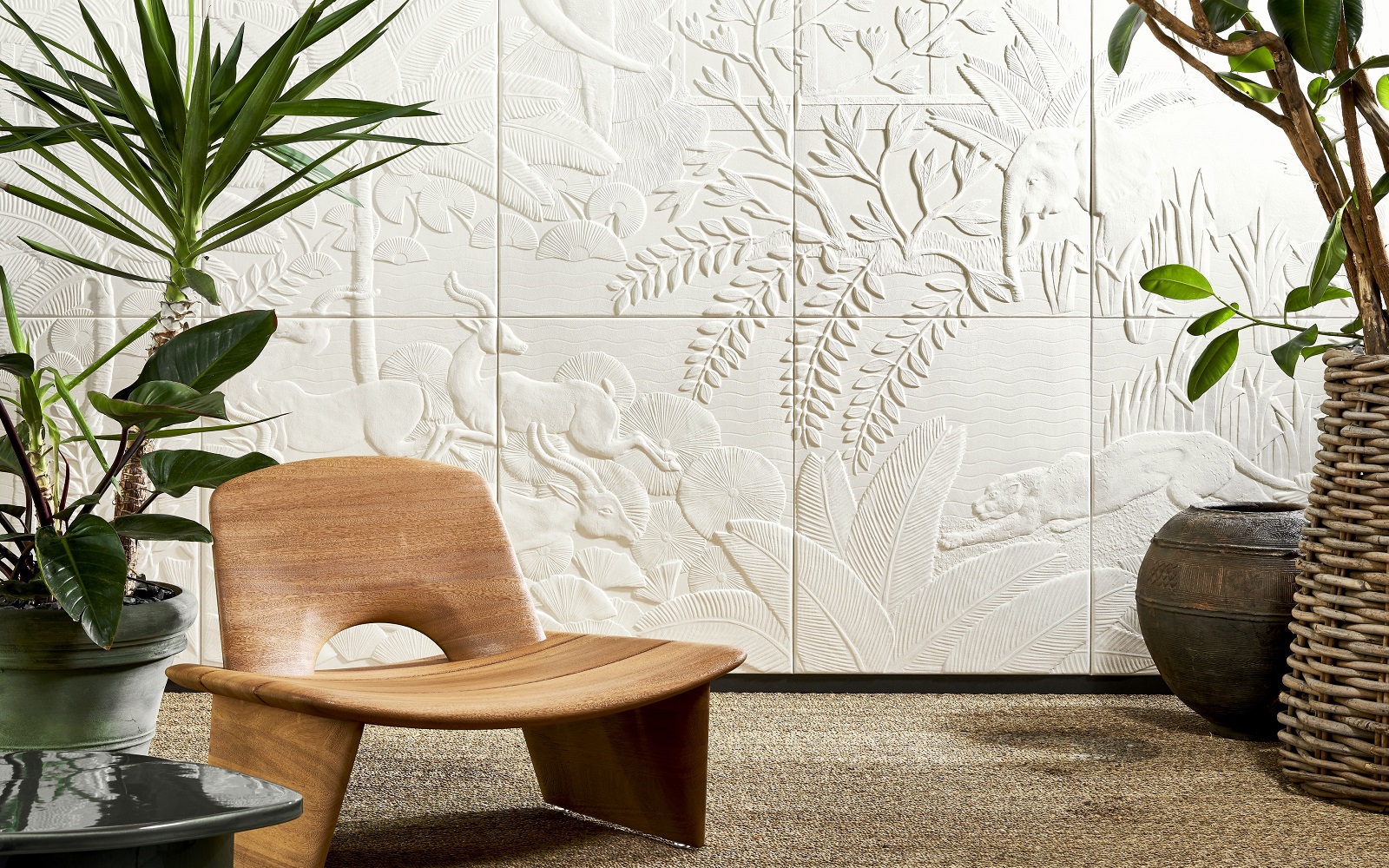 low wooden chair and plants in front of a relief design wallcovering in white showing plants and animals from the mythical babylon by Arte