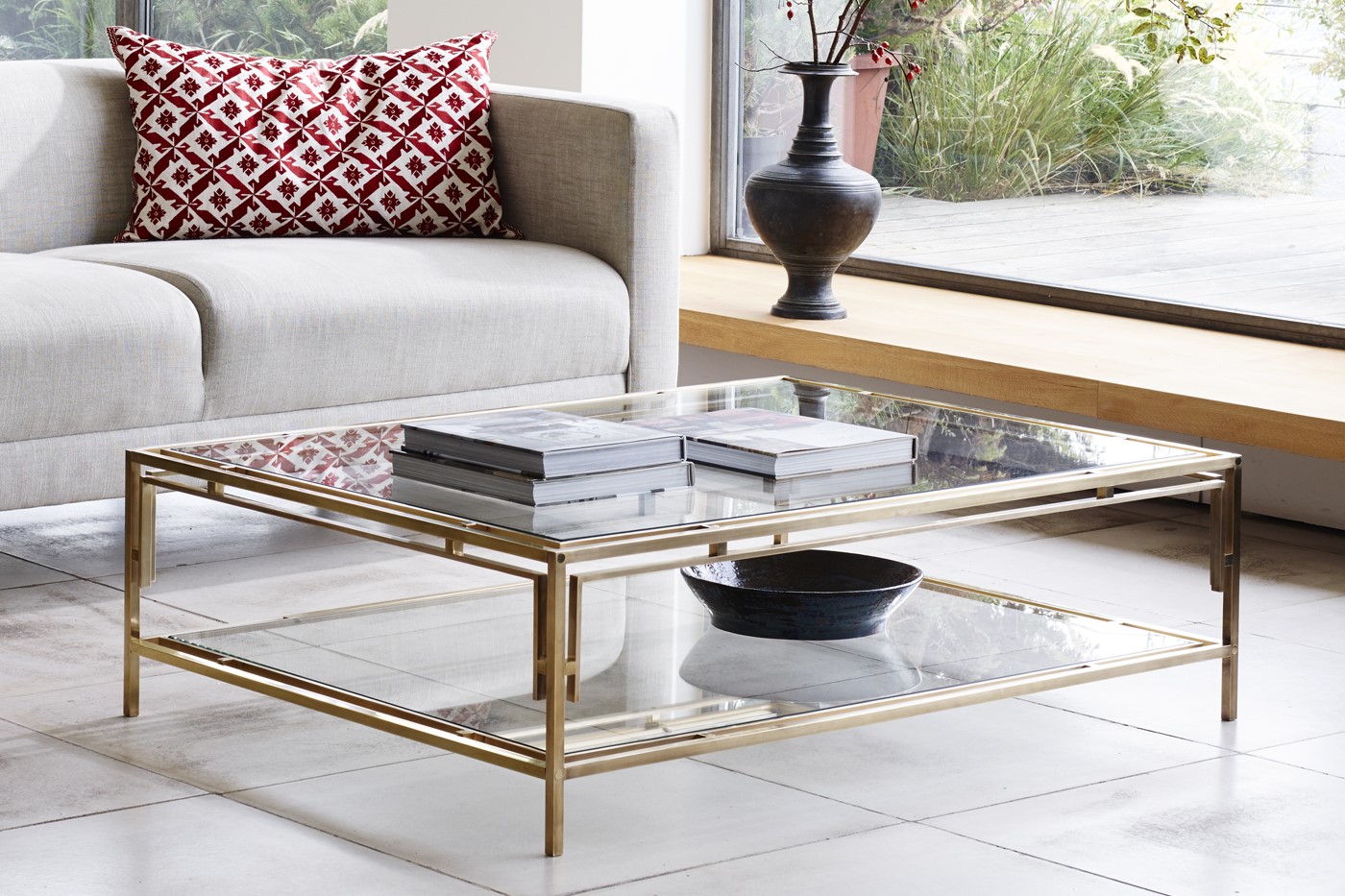 glass topped coffee table with books on it in front of cream couch with a rust patterned cushion