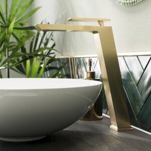 brushed brass mono basin tap above a white basin on a wooden surface with plants in the background
