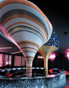 curved vortex shaped pillar covered in striped mosaic rising up from behind a curved bar