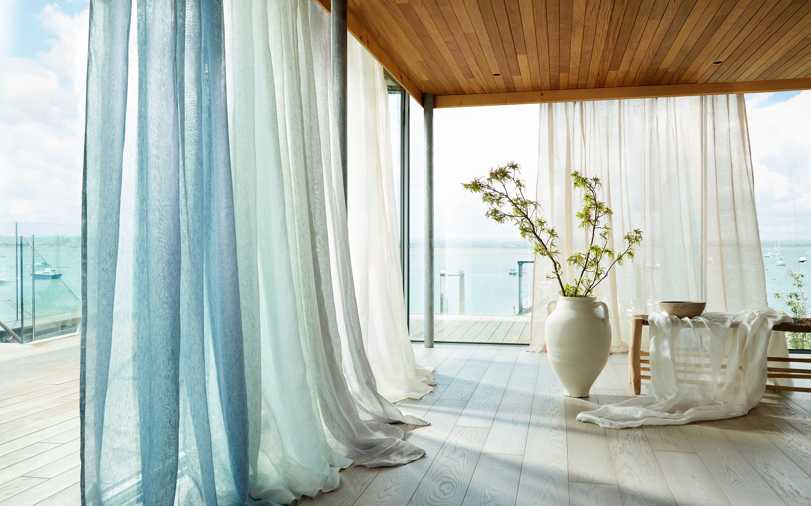 room with glass doors leading onto balcony overlooking the sea and sheer floor to ceiling curtains in Harlequin Sheer