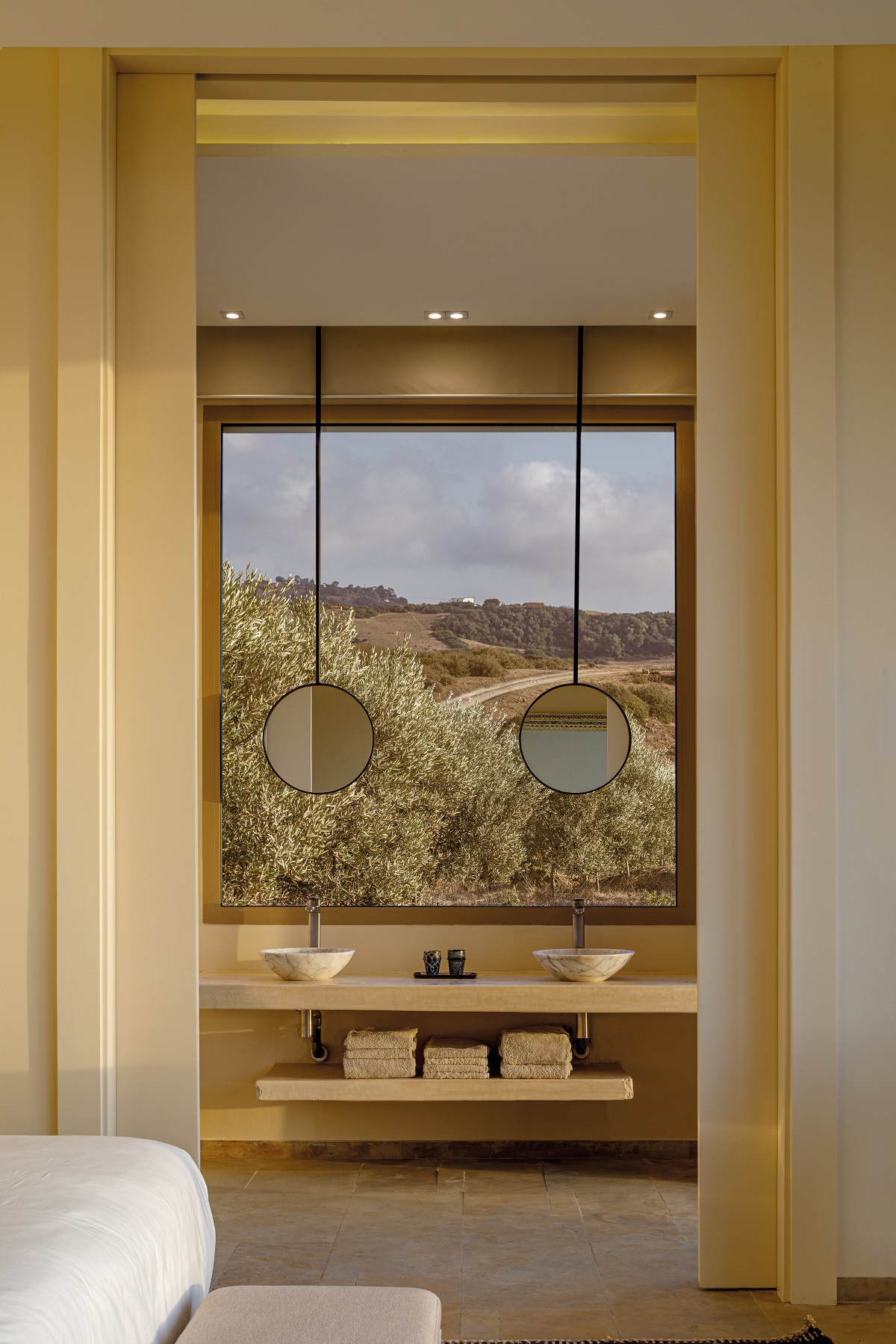 two round mirrors suspended in front of window in the bathroom with view over olive groves