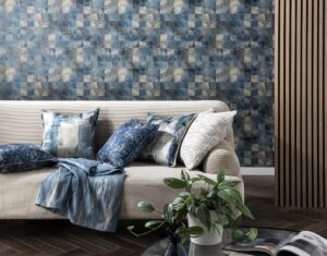 cream couch with a blue throw and a mix of cushions against blue and grey patterned wallpaper 