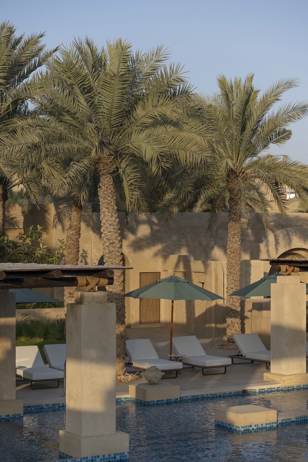 swimming pool surrounded by umbrellas, sun loungers and palm trees in a central courtyard of the hotel