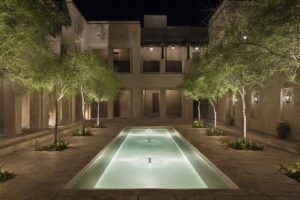 evening in central courtyard with palm trees on either side of arabic style pool with lighting and fountain