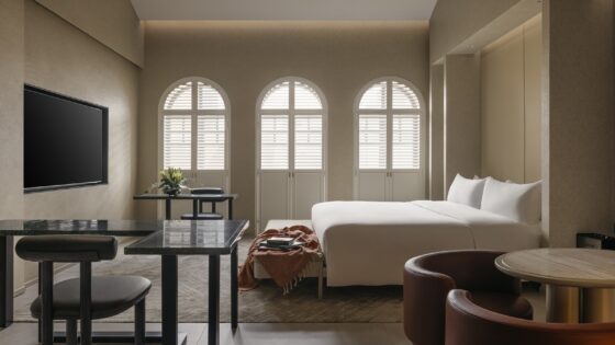 three arched shuttered windows in cream and white guestroom with wooden chair and table detail