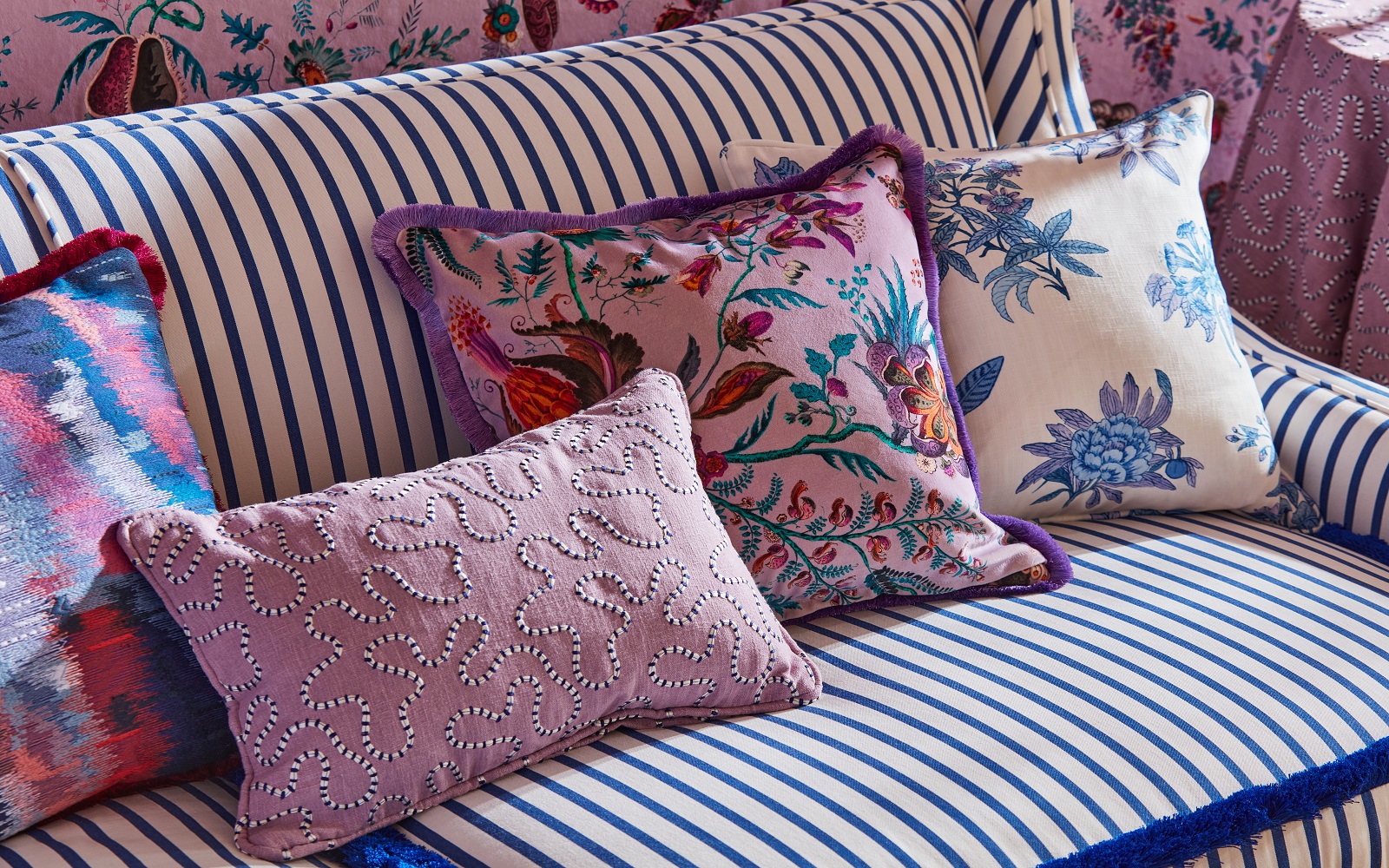 a colourful collection of patterned cushions on a striped sofa with fabrics from Harlequin x Sophie Robinson Collection